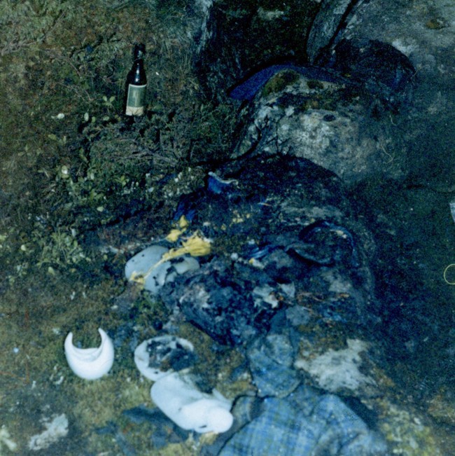Rare photo couleur de la scène. Son écharpe à carreaux bleus et verts, les bouteilles en plastique fondues et la bouteille de liqueur Kloster sont clairement visibles. | Photo de la police de Bergen