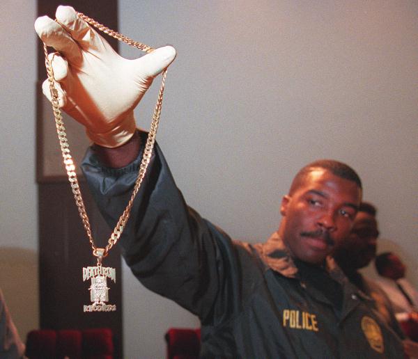 Un officier de police du LAPD tient un médaillon en or avec le symbole de Death Row. Les membres de l'étiquette portaient ce médaillon comme une forme de statut.